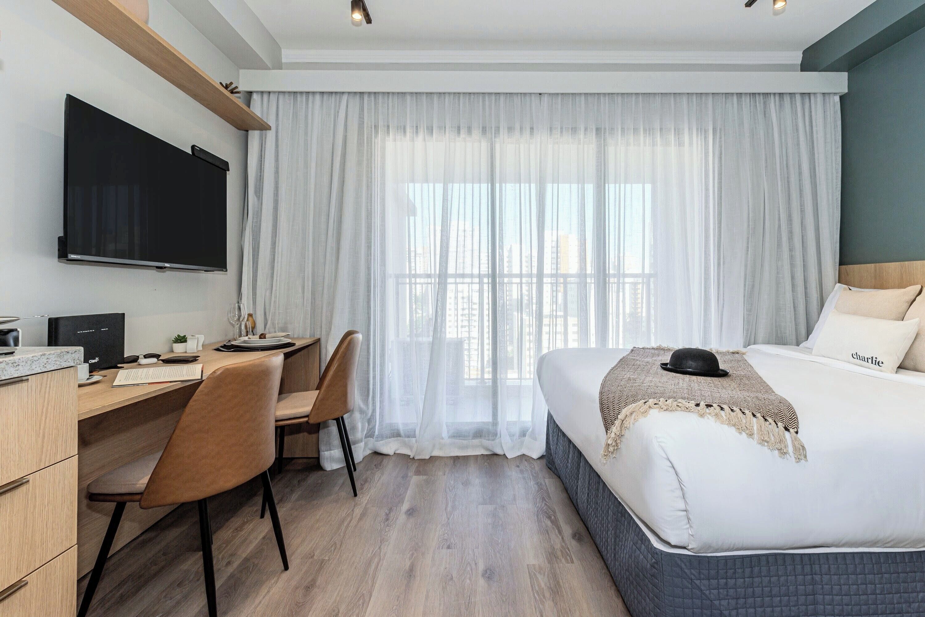 A hotel room with a bed, a desk, a chair, a TV, and a window with curtains.
