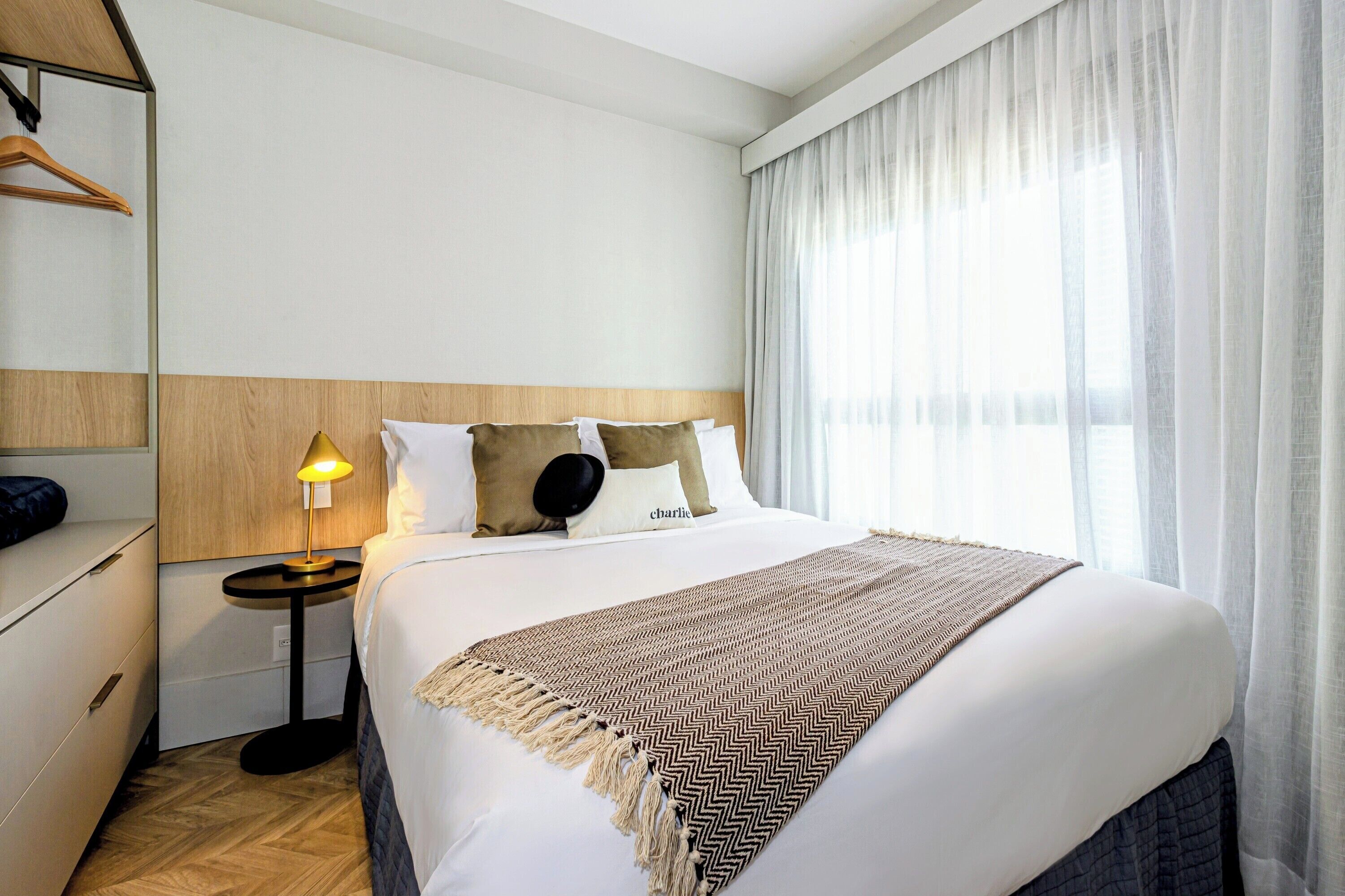 Ein Hotelzimmer mit einem Bett, einem Nachttisch mit Lampe, einem Kleiderschrank und einem Fenster mit Vorhängen.