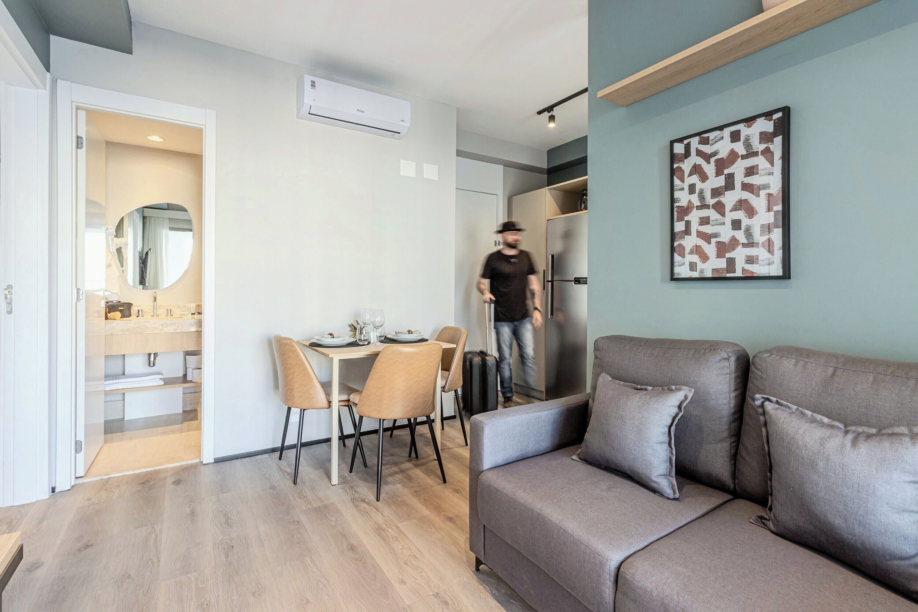 Una sala moderna con un sofá, una mesa de comedor con sillas, una zona de cocina con un refrigerador y un pasillo que lleva a un baño.