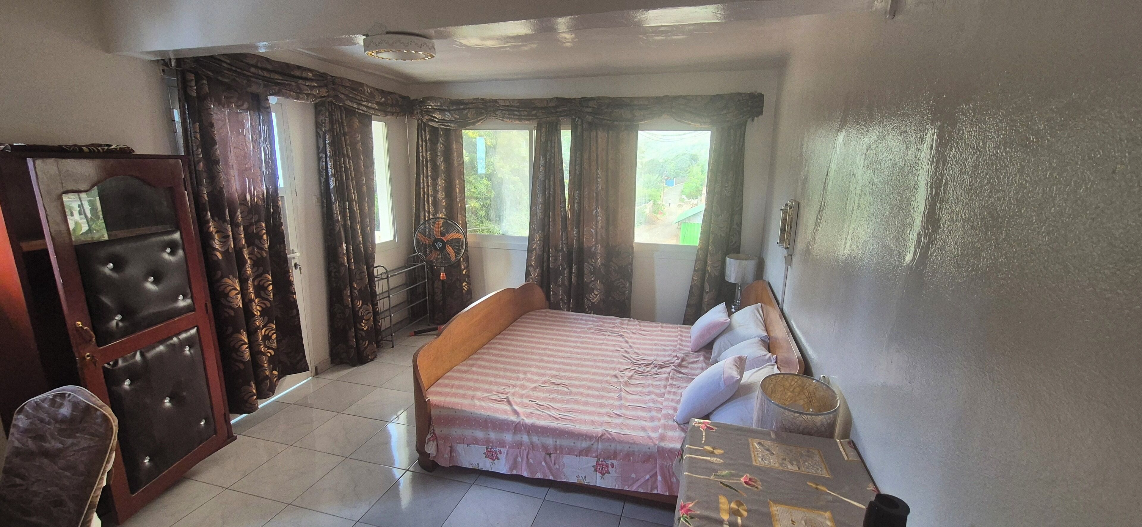 Ein Schlafzimmer mit Bett, Vorhängen, einem Ventilator, einem Schreibtisch und einem Stuhl.
