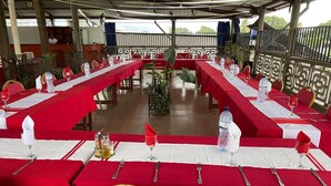 Ein Restaurant mit langen Tischen, gedeckten Plätzen, roten Tischdecken und goldenen Stühlen.