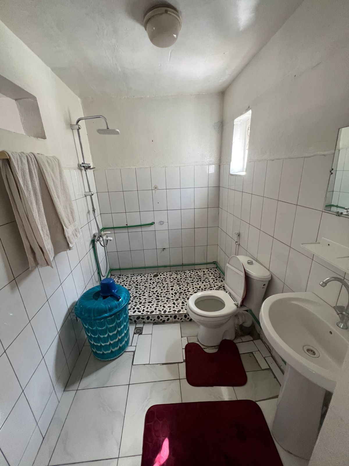 A small, tiled bathroom with a toilet, sink, shower, and a blue water container.