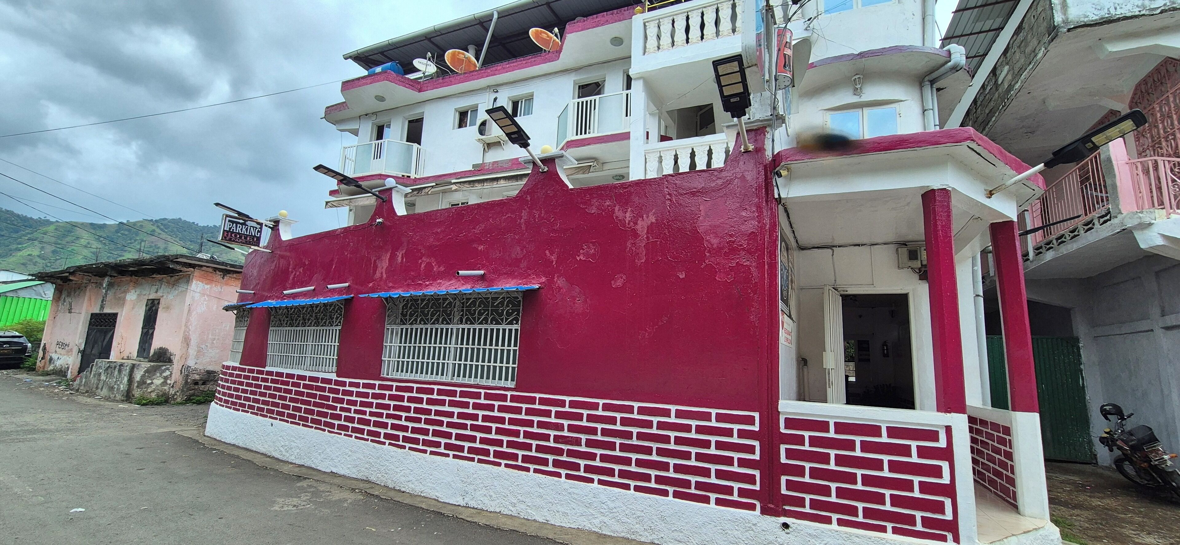 A multi-story building with a red and white facade, balconies, and satellite dishes.
