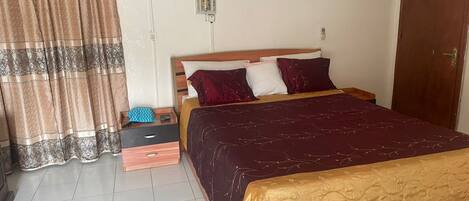 A bedroom with a bed, curtains, a nightstand, and a wooden drawer unit.