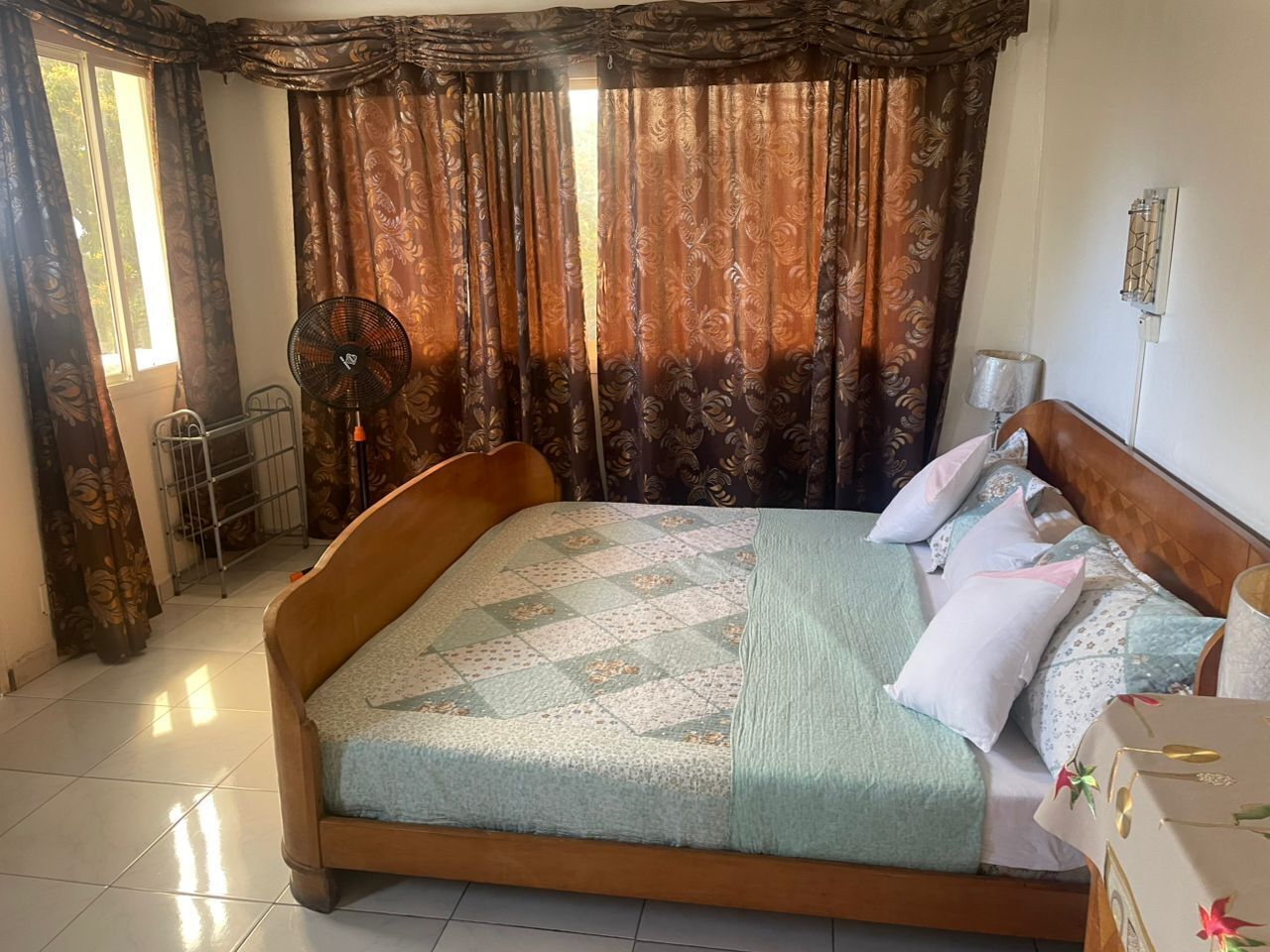A bedroom with a wooden bed, a patterned bedspread, and a fan.