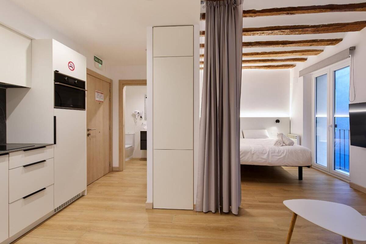 Een moderne hotelkamer met een bed, een klein tafeltje, een televisie en een badkamer die door een geopende deur zichtbaar is.