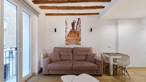 A modern living room with a brown sofa, a white coffee table, and a dining area with a white table and chairs. - Apartamentos Linda by Clabao (Pamplona)