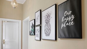 Un couloir avec des œuvres d’art encadrées accrochées au mur, une porte blanche et un luminaire.