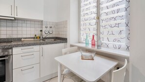 Une cuisine avec des meubles blancs, un plan de travail, un évier et une fenêtre agrémentée de rideaux à motifs.
