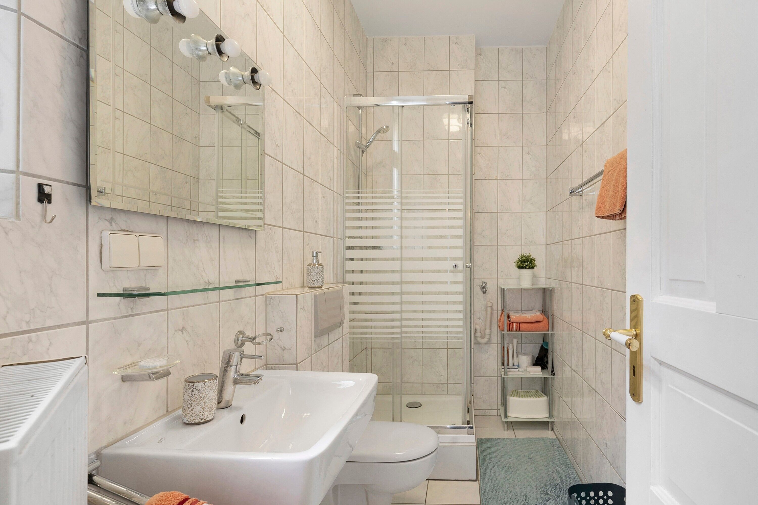 A bathroom with a sink, toilet, shower, and glass shelves.