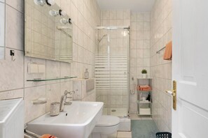 Un baño con lavamanos, inodoro, ducha y repisas de vidrio.