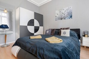 Un dormitorio moderno con una cama, una mesita de vidrio, una lámpara y una obra de arte en la pared.