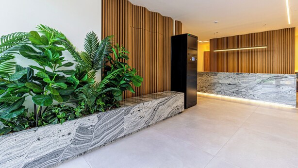 Una zona de recepción con mostrador de mármol, paneles de madera y abundante vegetación.