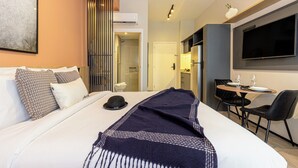 Habitación de hotel con una cama, una mesa de comedor con sillas, un televisor y un equipo de aire acondicionado.