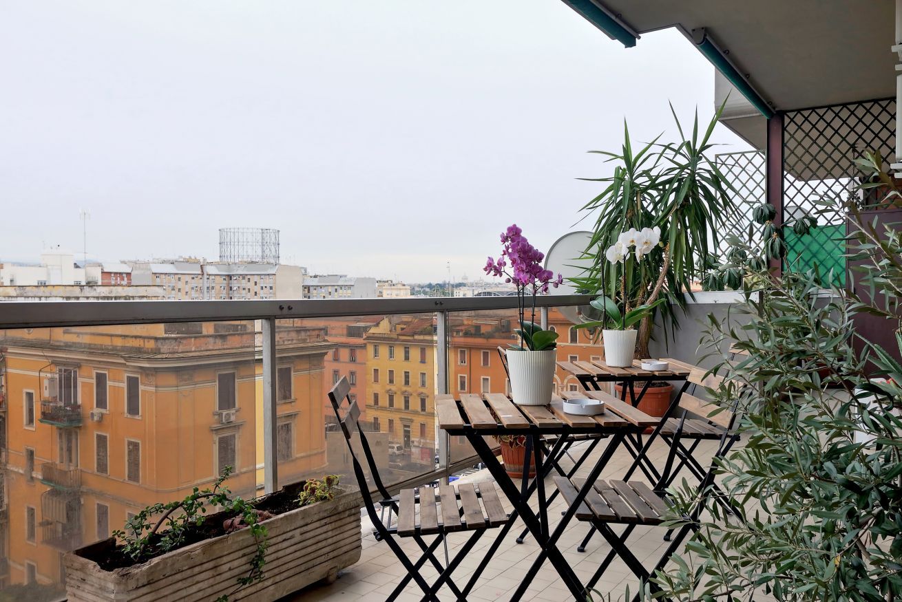 Un balcon avec une table et des chaises en bois, des plantes en pot et une vue sur les bâtiments de la ville.