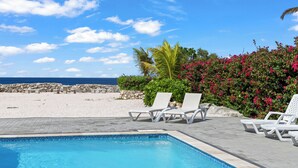 A poolside area with lounge chairs, a clear blue sky, and a view of the beach and ocean. - Ocean Hibiscus Punta Azul Resort  (Sabana Westpunt)