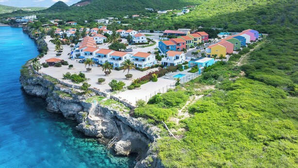 A coastal resort with colorful buildings, a swimming pool, and a rocky shoreline. - Ocean Hibiscus Punta Azul Resort  (Sabana Westpunt)