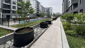 Een modern woongebouw met balkons, een zwembad en een aangelegde pad met potplanten.
