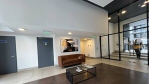 Een moderne lobby met een bruine leren bank, een glazen salontafel en een groot abstract schilderij aan de muur.