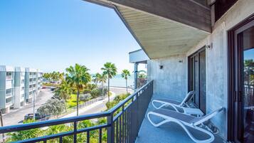 A balcony with a view of a road, palm trees, and a building across the street.