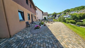 A paved courtyard with a brick pathway, a bench, and potted plants. - Wildgrund Apartment (Siegen Achenbach)