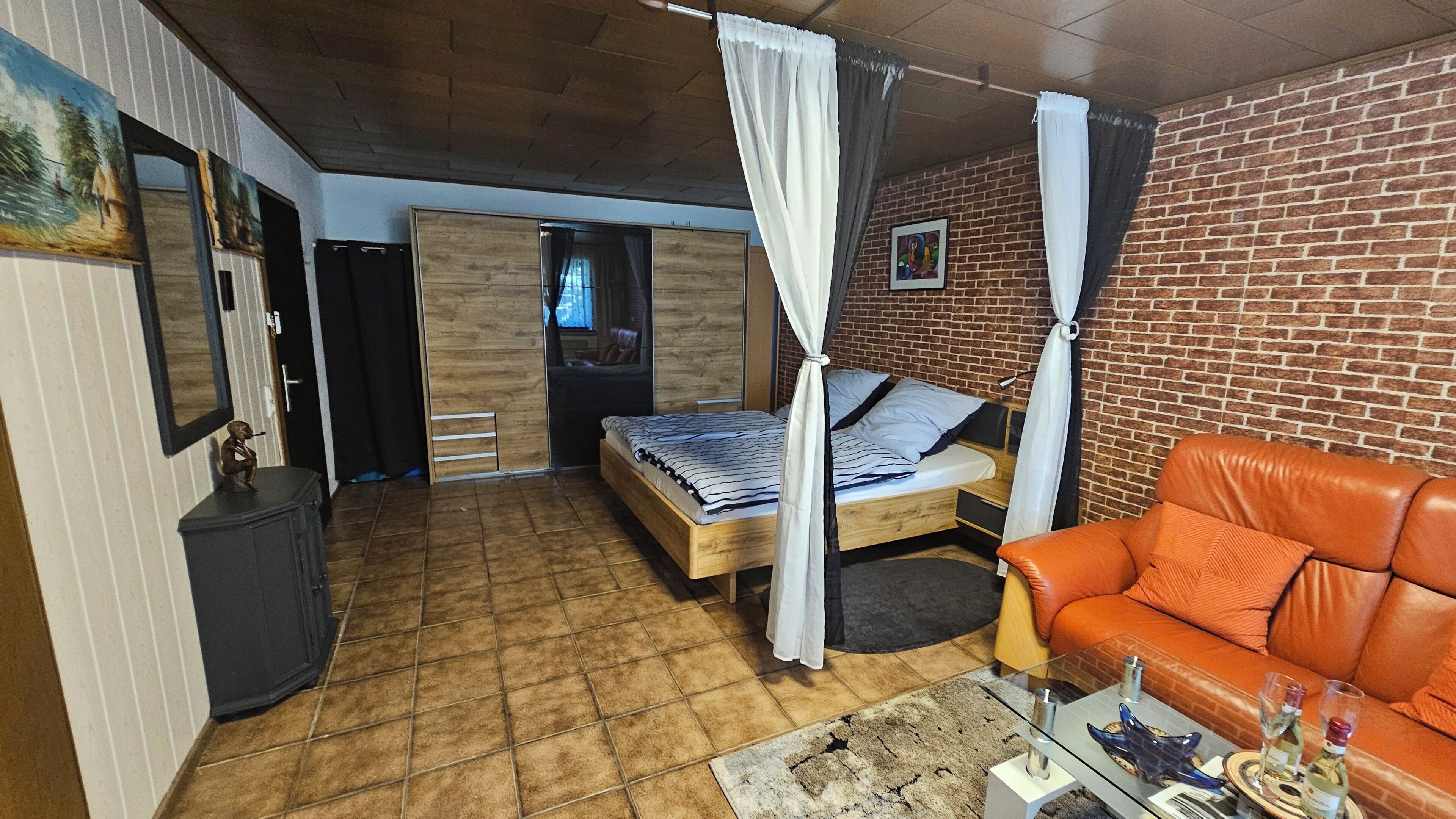 Una habitación con una cama, un sofá, una mesita con vasos y una pared de ladrillo.