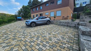 A paved driveway leading to a two-story building with a car parked in the driveway. - Wildgrund Apartment (Siegen Achenbach)