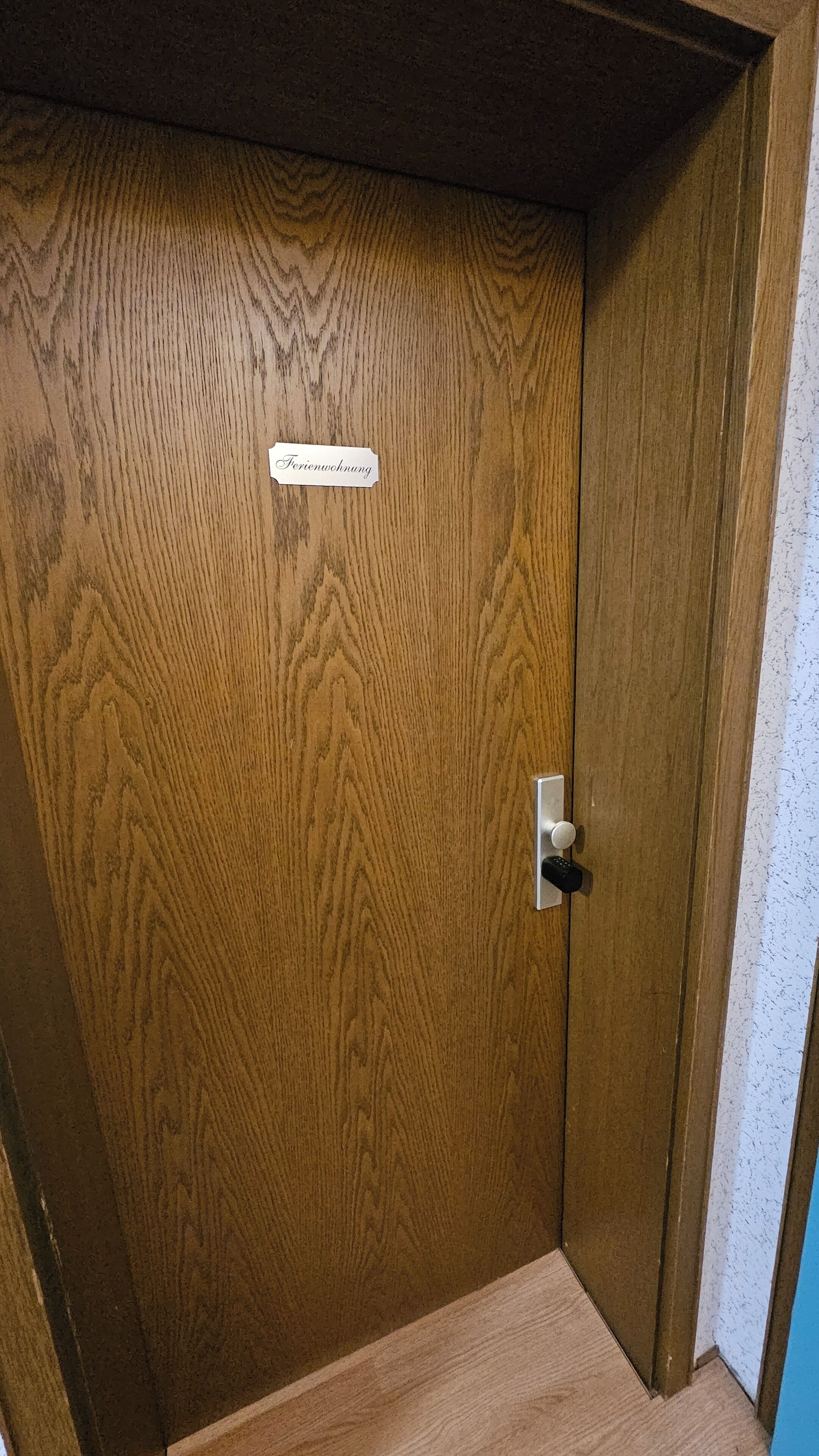 Een houten deur met een bord waarop 'Ferienswohnung' staat en een sleutelgat.
