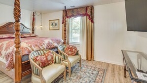 Un dormitorio con una cama con dosel, dos sillones tapizados, una mesa de vidrio y una alfombra estampada.