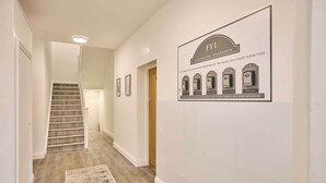 A hallway with a staircase leading to another floor, a framed signboard with apartment names, and a rug on the floor.