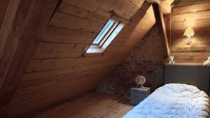 Una stanza piccola con tetto spiovente, pareti in legno, un letto singolo, un comodino, un tavolino con un oggetto decorativo e una finestra.