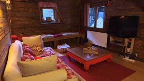 Un accogliente interno di una baita con un divano, un tavolino, una televisione e una finestra con vista.