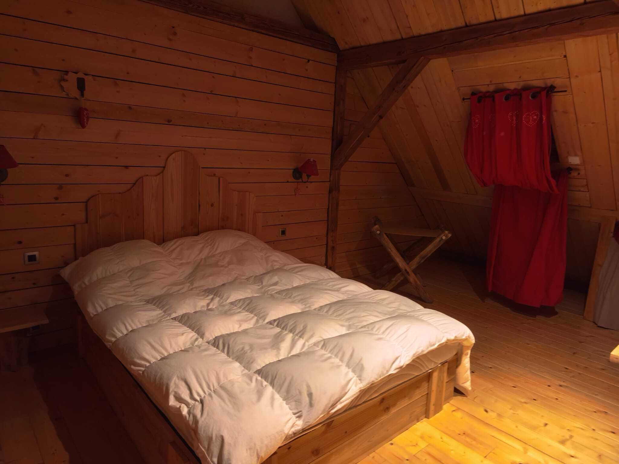 Una habitación de cabaña de madera con una cama, una mesita pequeña y una cortina roja.