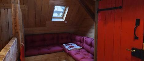 Una habitación acogedora en el ático, con techo de madera, una puerta roja y un tragaluz pequeño.