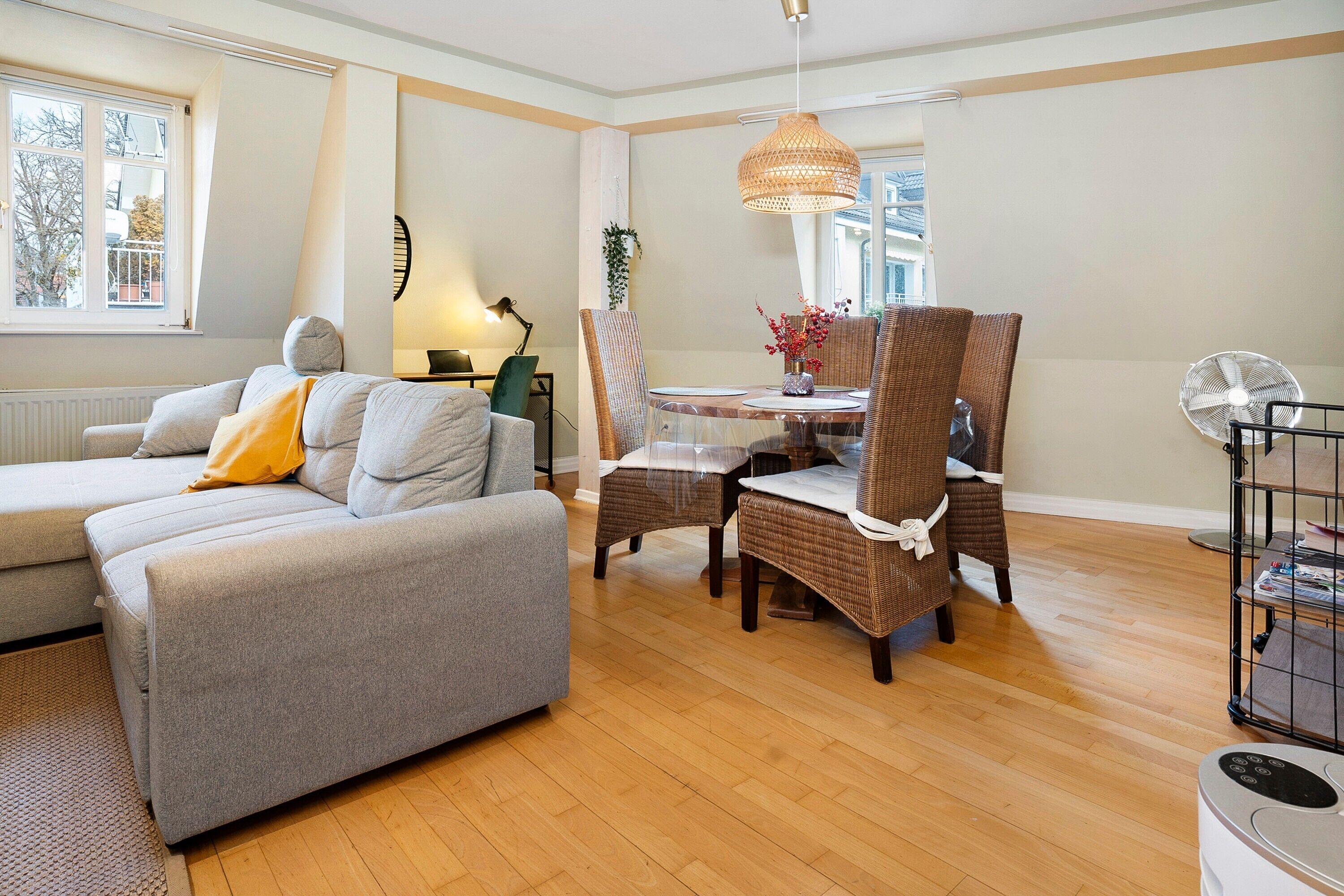 A modern living room with a sofa, dining table, wicker chairs, and a ceiling fan.