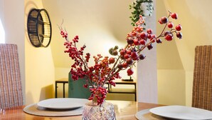 Una mesa de comedor con un florero de vidrio con bayas rojas, dos platos blancos y posavasos tejidos.