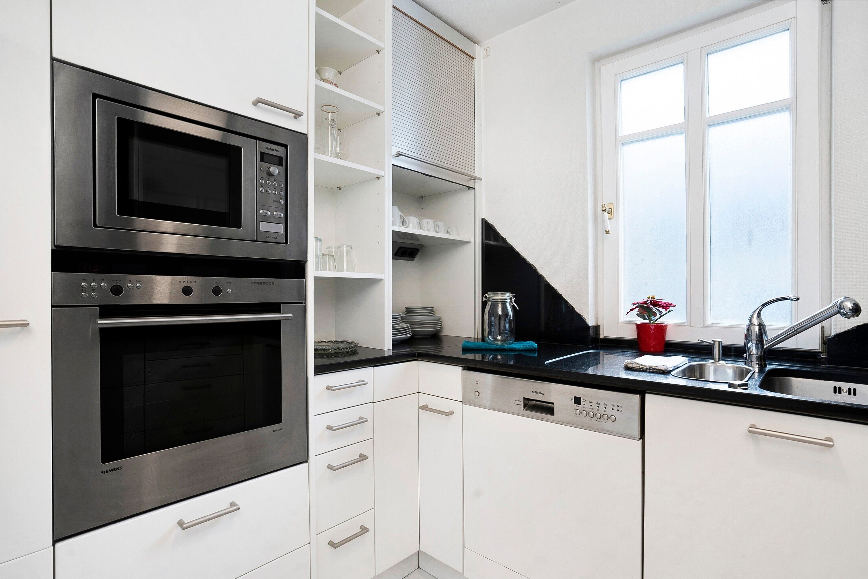 A modern kitchen with a built-in microwave, oven, and dishwasher, a black countertop, and a window above the sink.