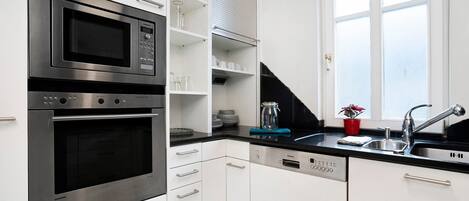 A modern kitchen with a built-in microwave, oven, and dishwasher, a black countertop, and a window above the sink.