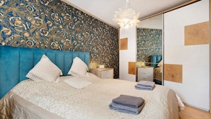 Un dormitorio con una cama grande, cabecera, mesita de noche, cómoda y espejo.