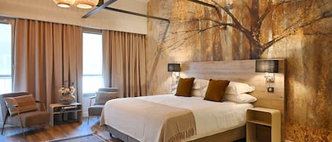 A modern bedroom with a large bed, a wooden headboard, and a wall mural. There are two bedside tables with lamps, a chair, and a rug.
