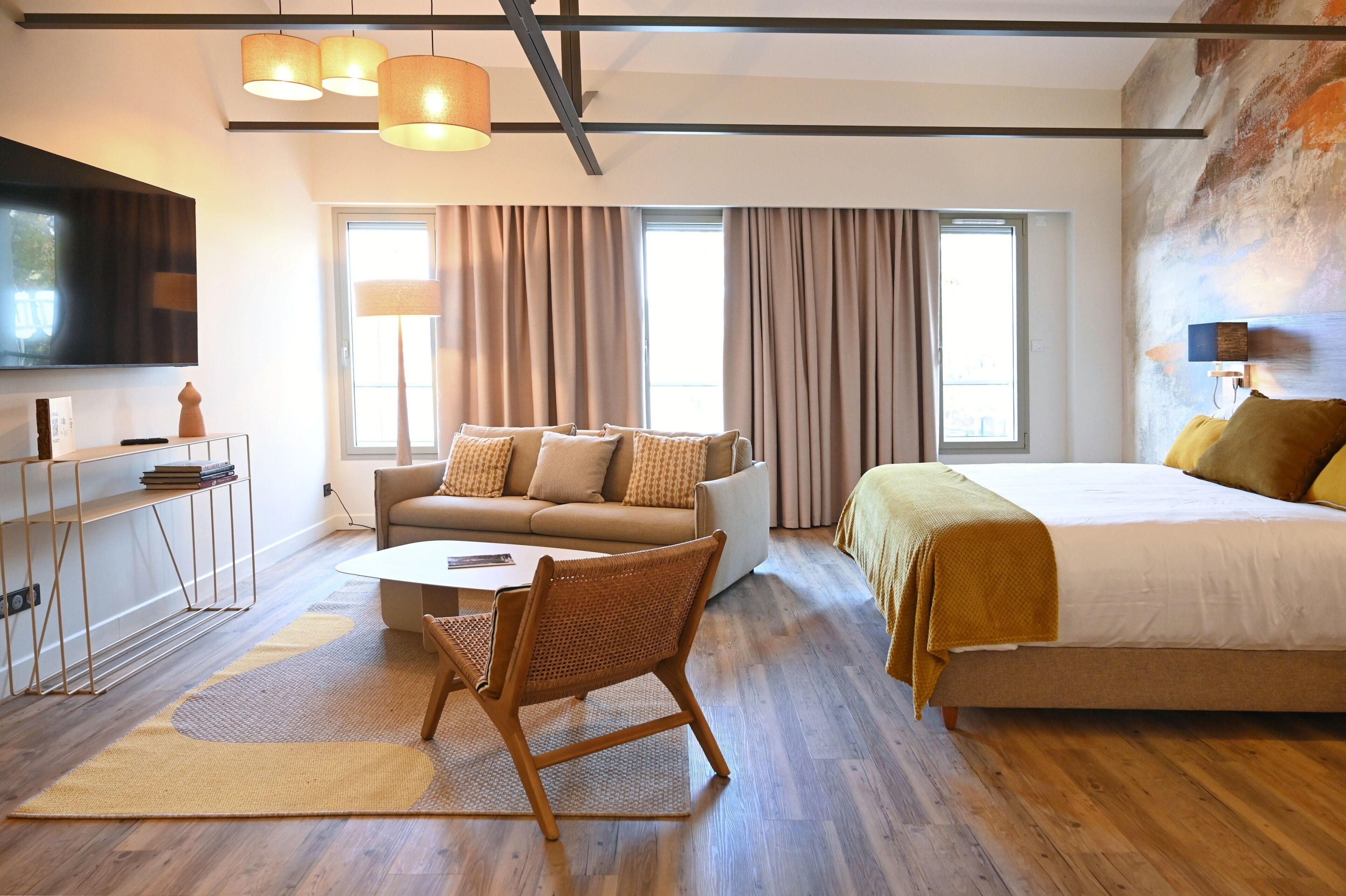 Ein modernes Hotelzimmer mit einer Couch, einem Bett, einem Fernseher und einem Schreibtisch mit einer Lampe.