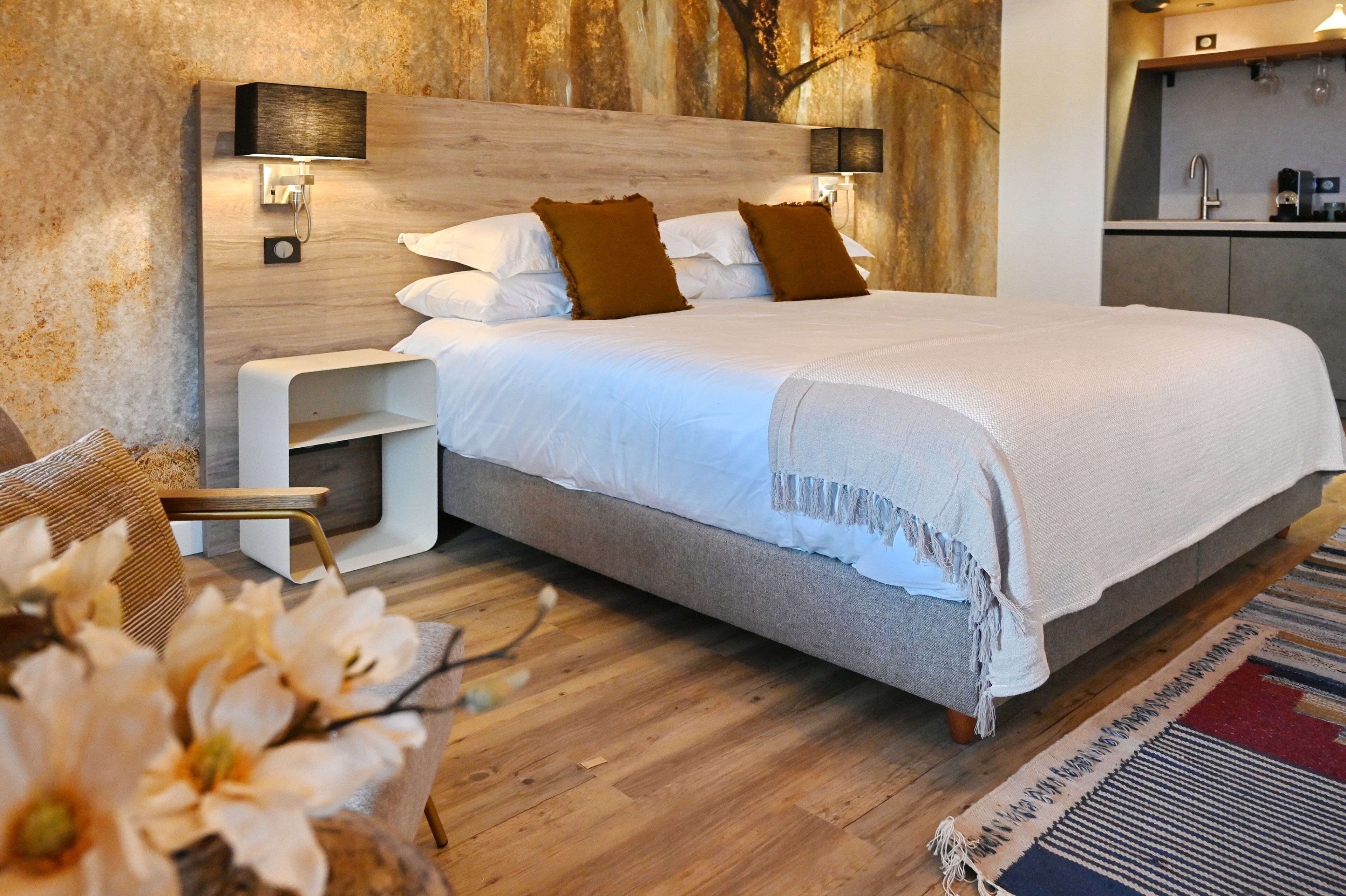 A modern bedroom with a wooden headboard, a bedside table, a built-in shelf, and a large bed with white bedding and brown pillows.