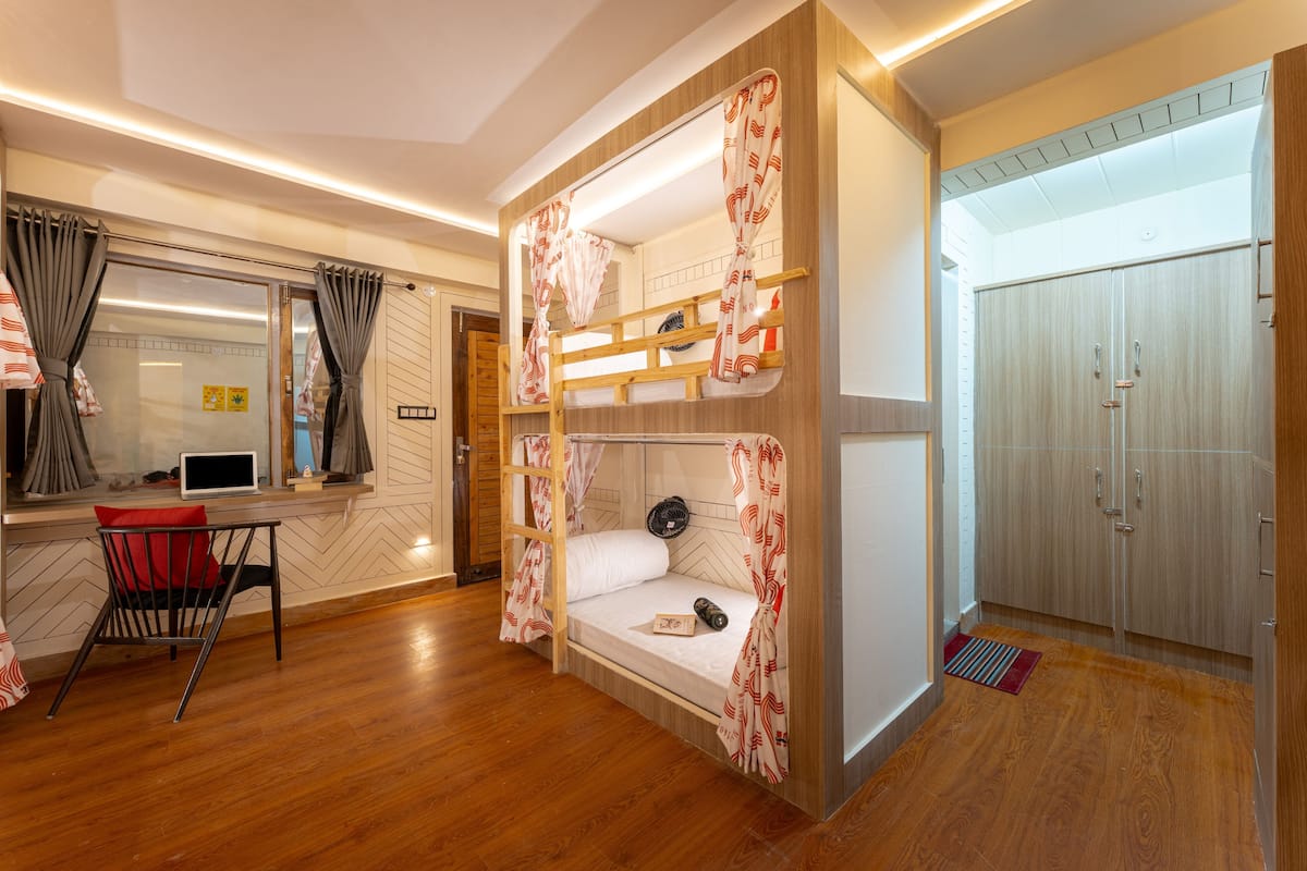 A bunk bed room with a desk and chair, wooden flooring, and a wardrobe.
