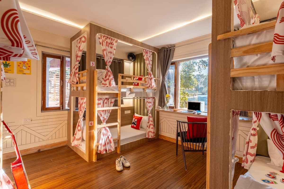 A room with bunk beds, a desk with a computer, and a window with a view of trees.
