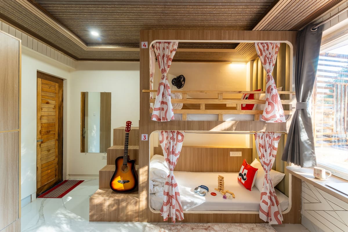 A bunk bed room with a guitar, a mirror, and a window with curtains.