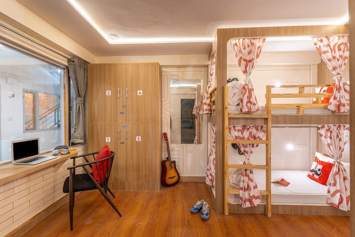 A room with bunk beds, a desk with a laptop, a guitar, and a chair with a red cushion.