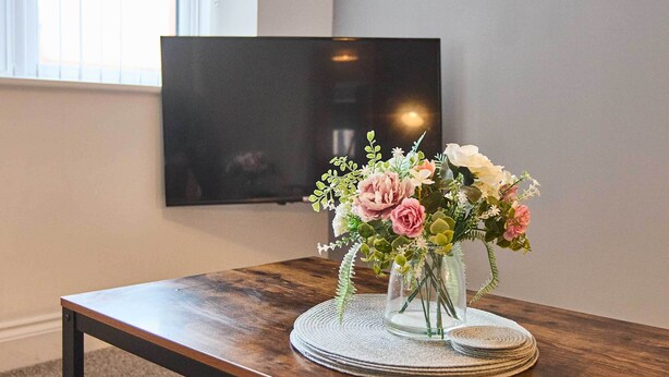 A wooden table with a glass vase containing flowers, placed on a woven placemat.