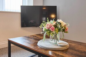 Een houten tafel met een glazen vaas vol bloemen, geplaatst op een geweven placemat.