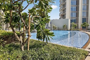 A swimming pool with a curved edge, surrounded by greenery and a modern building in the background. - Spa / Gym / Sea View / High Floor / Marina Walk (Dubai)