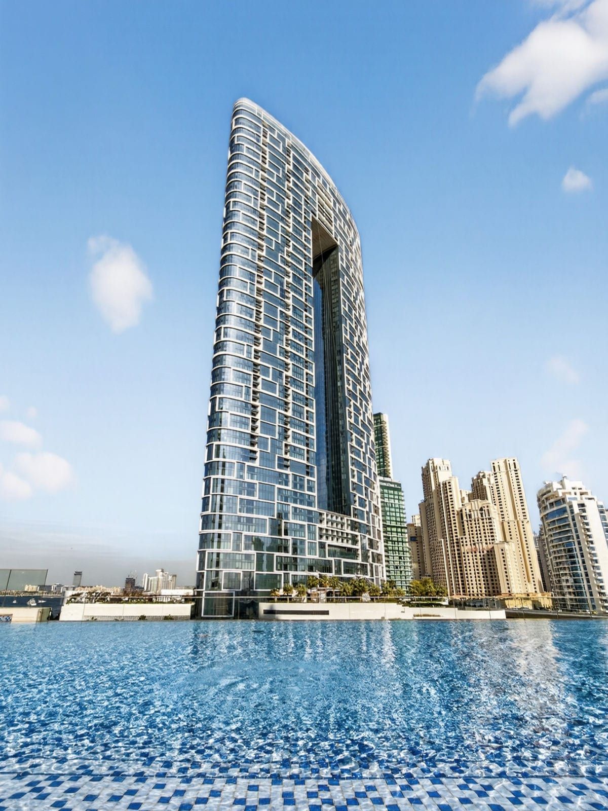 Un hôtel de grande hauteur, doté d’une façade incurvée remarquable, avec une piscine en premier plan et d’autres bâtiments environnants.